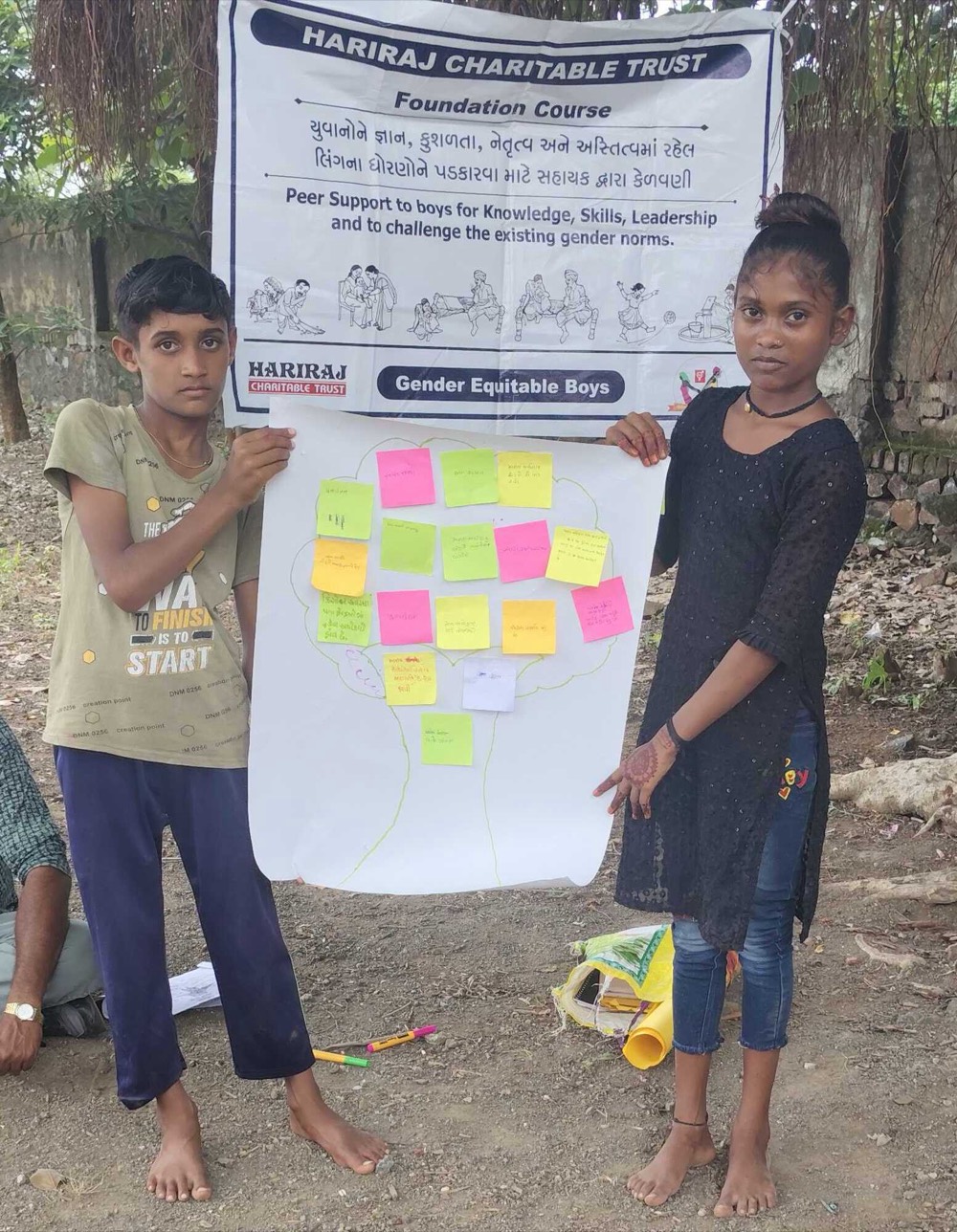 Two adolescents holding up a chart of coloured sticky notes in front of a Gender Equitable Boys foundation course banner