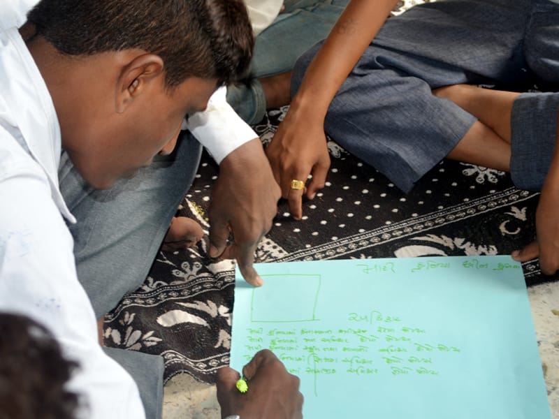 Hands of adolescent boys working together on a handwritten chart spread on a mat