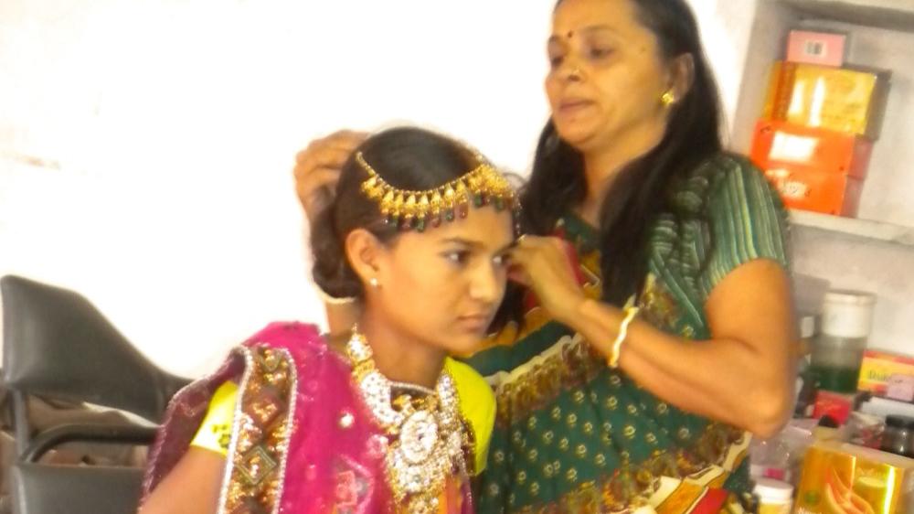 A trainer arranging jewellery in the hair of a young woman seated in a beauty parlour chair, during a bridal make-up practical